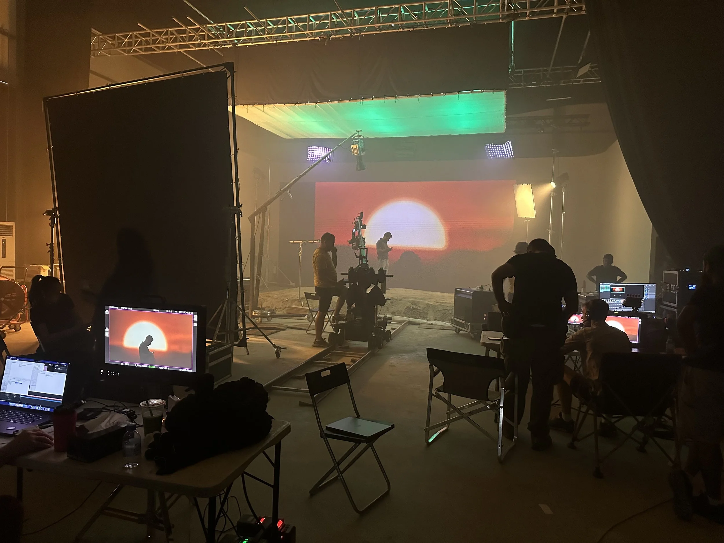 Production crew filming a sunset scene with camera track and overhead lighting